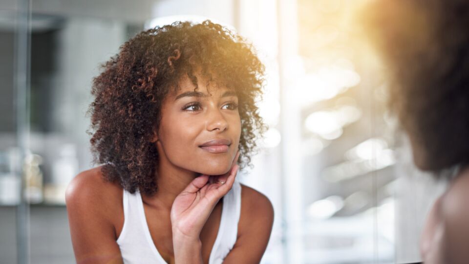 Woman looking in mirror with a soft smile and touching her face